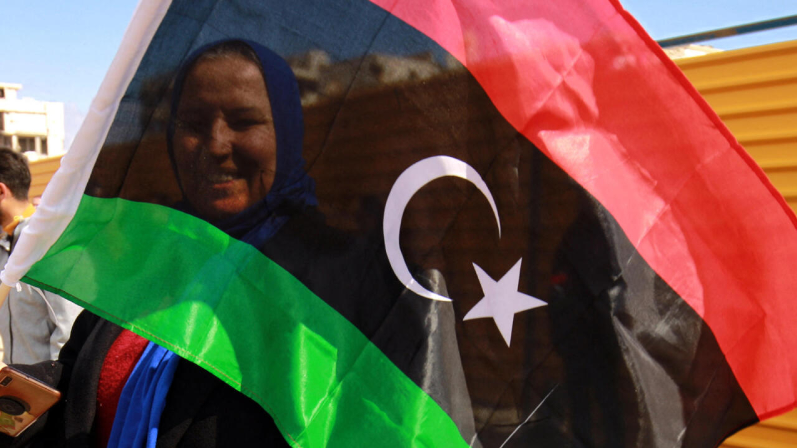 A woman waves a national flag as Libyans mark the 10th anniversary of the 2011 revolution, in the eastern city of Benghazi, on February 17, 2021. - The uprising toppled longtime ruler Moamer Kadhafi, ending a long-lived dictatorship but throwing the country into a decade of violent lawlessness. (Photo by Abdullah DOMA / AFP)